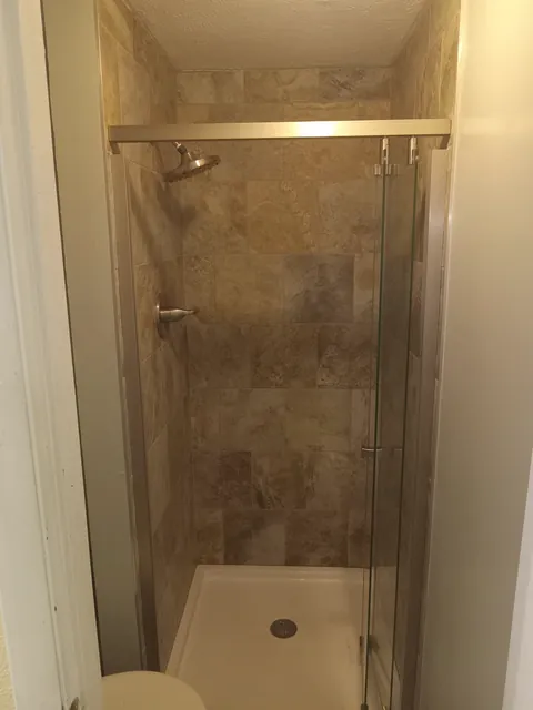 Glass shower enclosure with brown wall panels and a white shower base