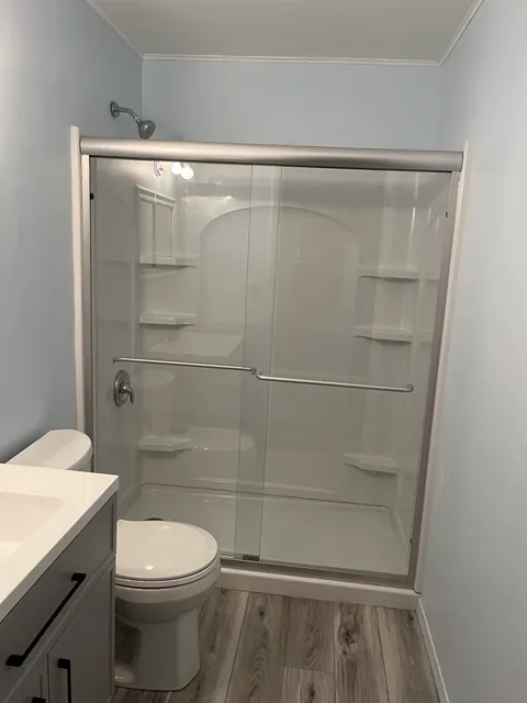 Glass shower enclosure with gray walls and wood look flooring
