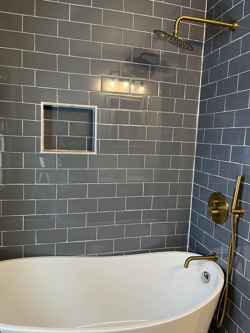 White tub with gold colored fixtures and gray tile