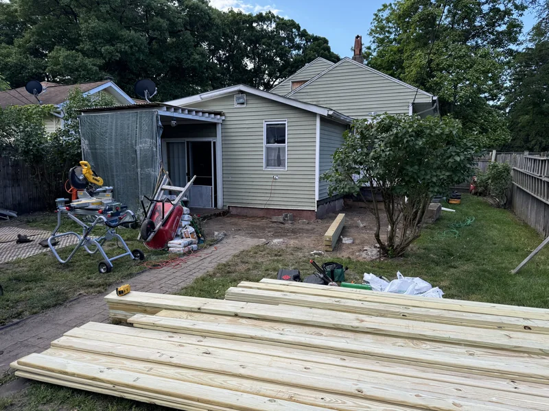 Exterior work area with stacked lumber and tools beside the house